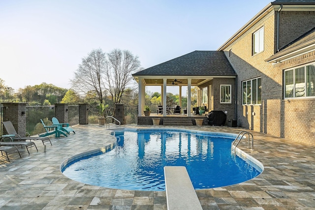 view of swimming pool featuring a fenced in pool, fence, a ceiling fan, a patio area, and a diving board