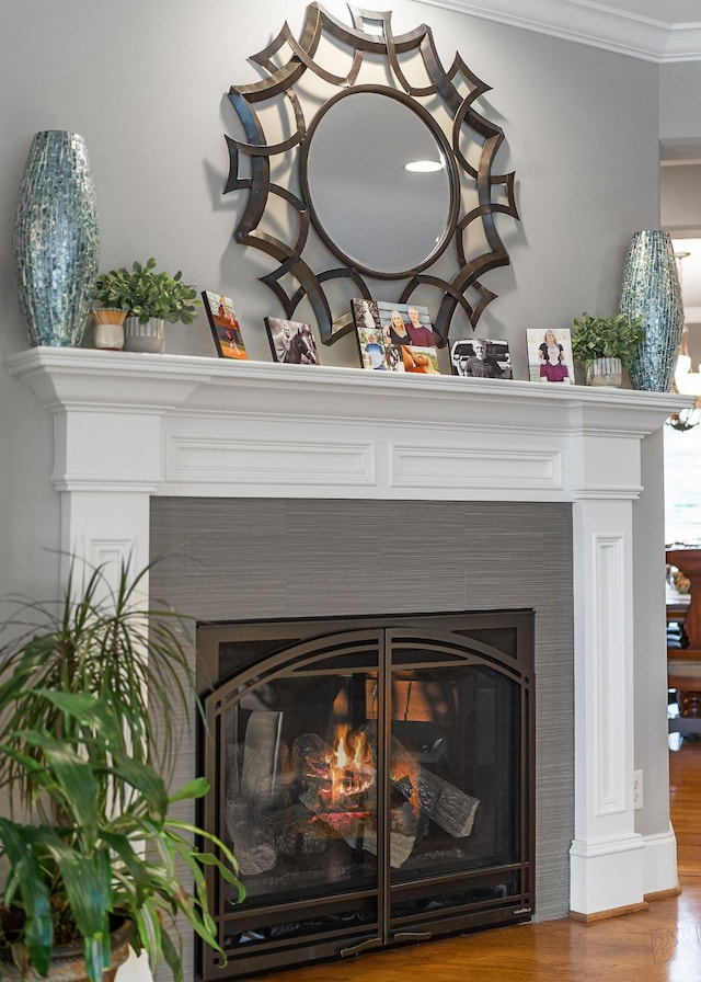 interior details featuring wood finished floors, ornamental molding, and a lit fireplace