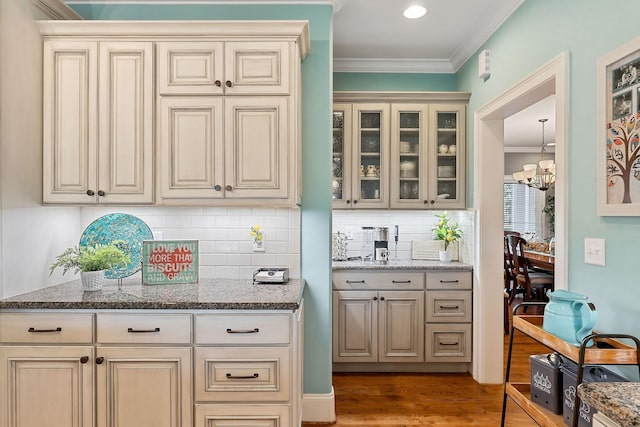 bar featuring backsplash, wood finished floors, crown molding, and a notable chandelier
