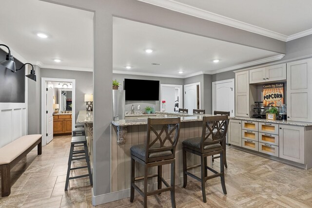 kitchen featuring a kitchen breakfast bar, light stone countertops, crown molding, and stone tile floors