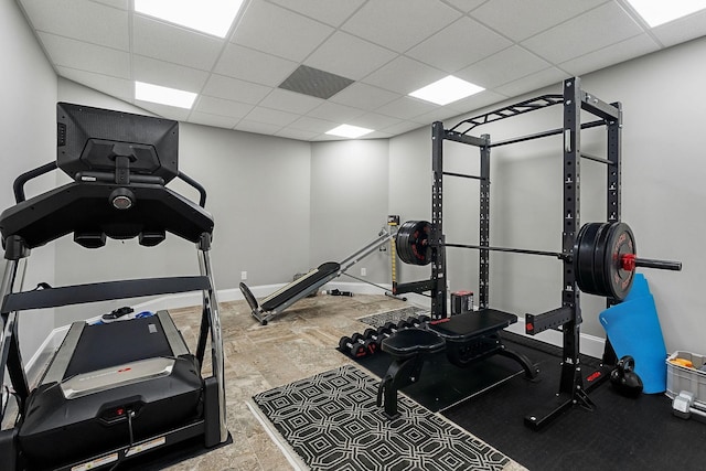 workout room featuring a paneled ceiling, stone finish flooring, and baseboards