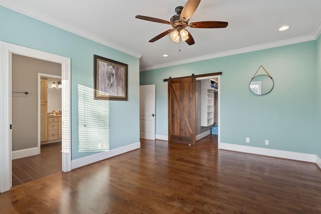 unfurnished bedroom with a barn door, a spacious closet, wood finished floors, ornamental molding, and baseboards