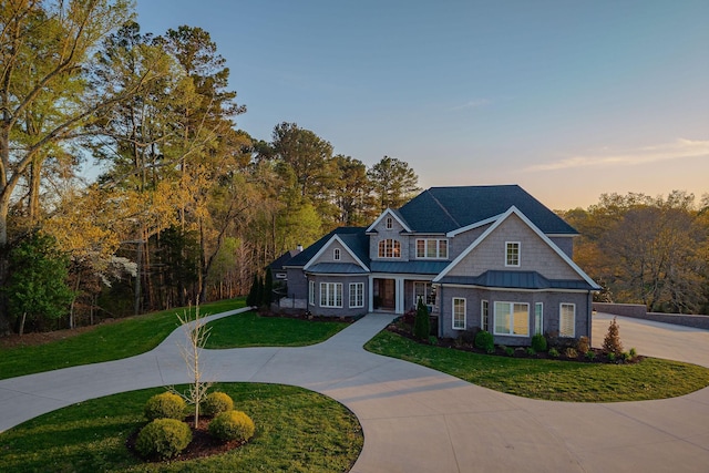 view of front facade with a standing seam roof, a front yard, curved driveway, and metal roof