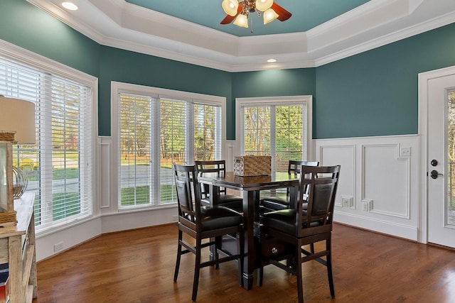 dining room featuring dark wood-style floors, a raised ceiling, ceiling fan, a decorative wall, and ornamental molding