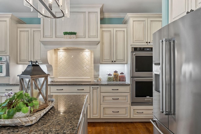 kitchen with cream cabinets, decorative backsplash, dark stone counters, and stainless steel appliances