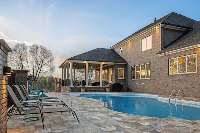 pool at dusk with fence, a patio area, a fenced in pool, and ceiling fan