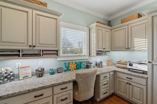 kitchen with built in desk, cream cabinets, dark wood finished floors, ornamental molding, and light stone countertops