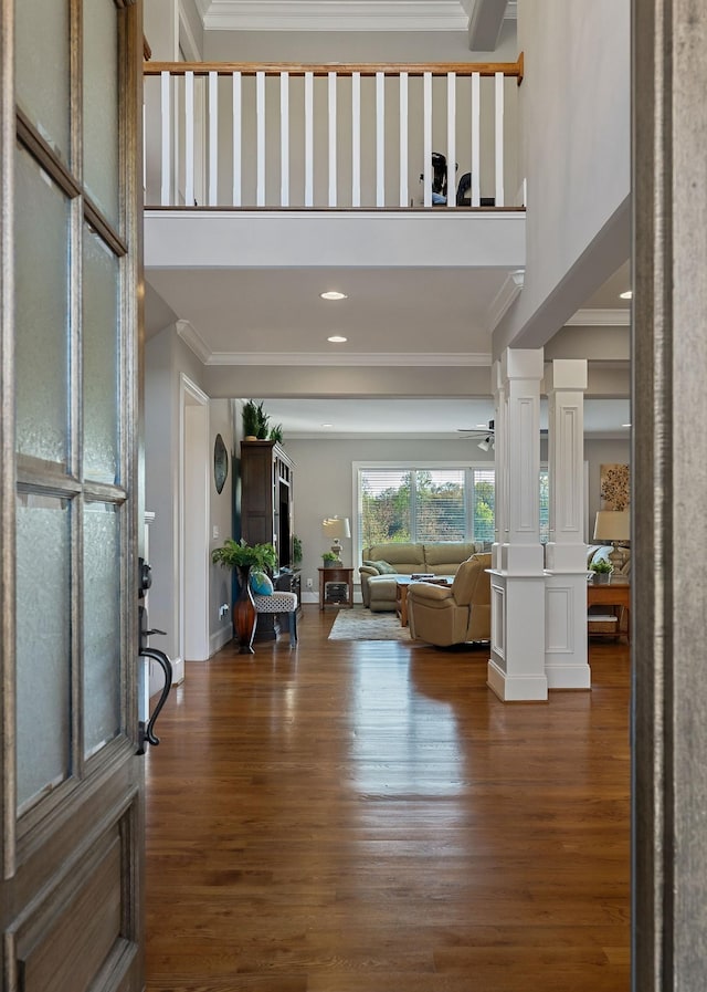 entryway featuring wood finished floors, a towering ceiling, ornate columns, and ornamental molding
