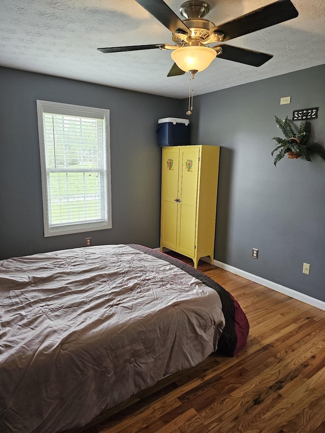 bedroom featuring baseboards, a ceiling fan, wood finished floors, and a textured ceiling
