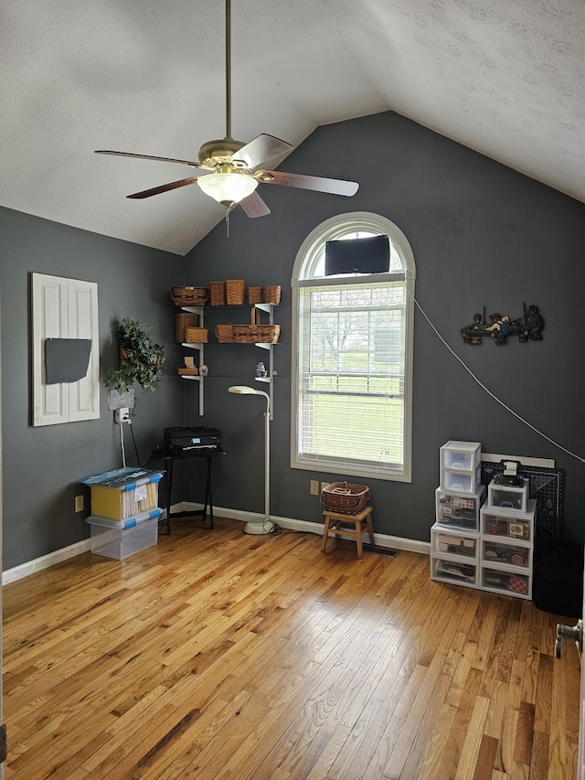 interior space featuring vaulted ceiling, a ceiling fan, wood-type flooring, baseboards, and a textured ceiling