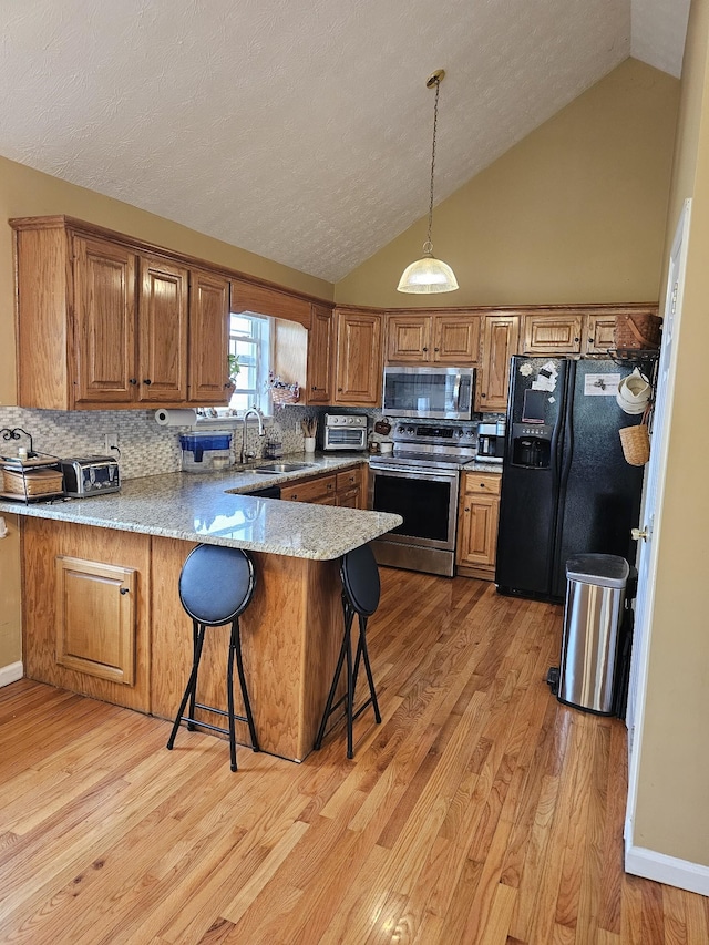 kitchen with brown cabinetry, a peninsula, stainless steel appliances, and a sink