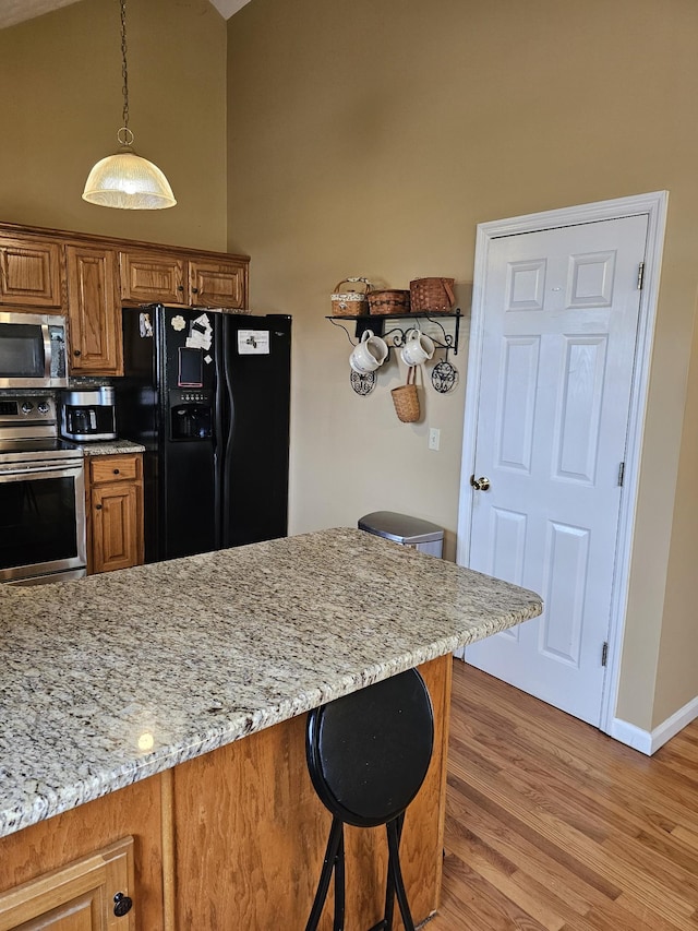kitchen featuring light stone counters, a breakfast bar, light wood-style floors, brown cabinetry, and appliances with stainless steel finishes