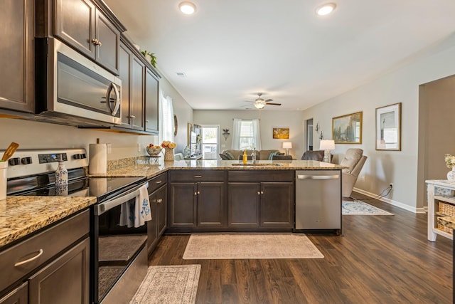 kitchen featuring stainless steel appliances, a peninsula, a sink, dark brown cabinets, and dark wood-type flooring