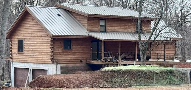 exterior space with an attached garage, covered porch, log siding, and metal roof