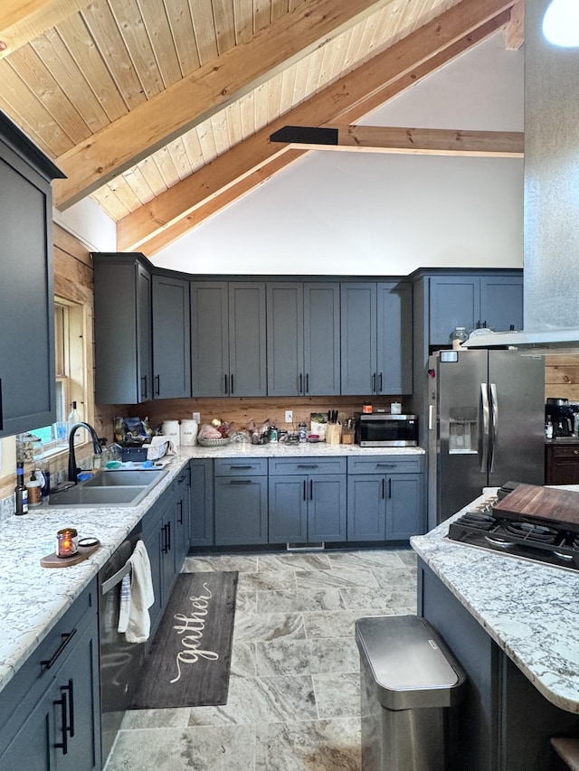 kitchen with a sink, vaulted ceiling with beams, wooden ceiling, appliances with stainless steel finishes, and stone finish floor