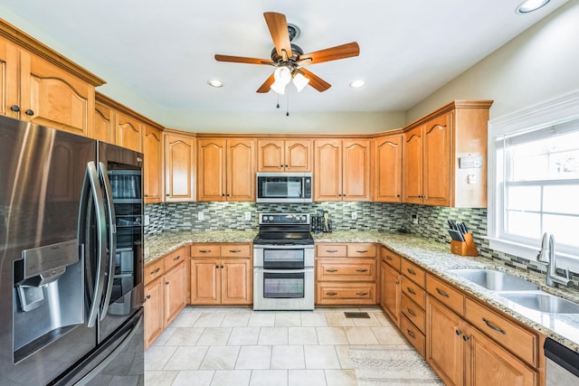 kitchen featuring light stone countertops, appliances with stainless steel finishes, a sink, a ceiling fan, and tasteful backsplash
