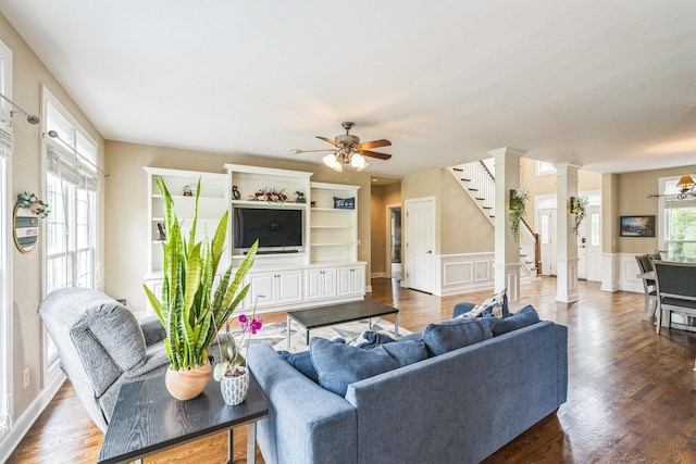 living room with stairs, decorative columns, a decorative wall, ceiling fan, and a wainscoted wall