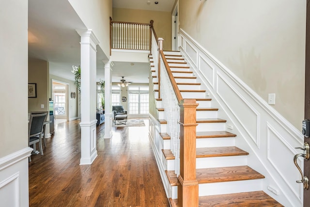 stairway featuring ceiling fan, decorative columns, wood finished floors, and a towering ceiling
