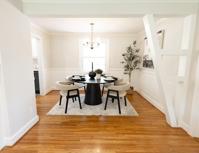 dining area with ornamental molding, a decorative wall, a wainscoted wall, light wood-style flooring, and a notable chandelier