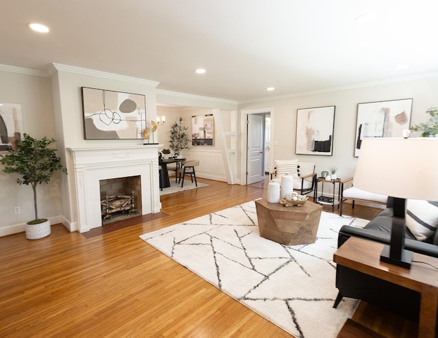 living room featuring recessed lighting, a fireplace with flush hearth, ornamental molding, and light wood finished floors