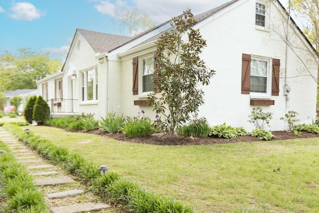 view of property exterior with a yard, brick siding, and a shingled roof