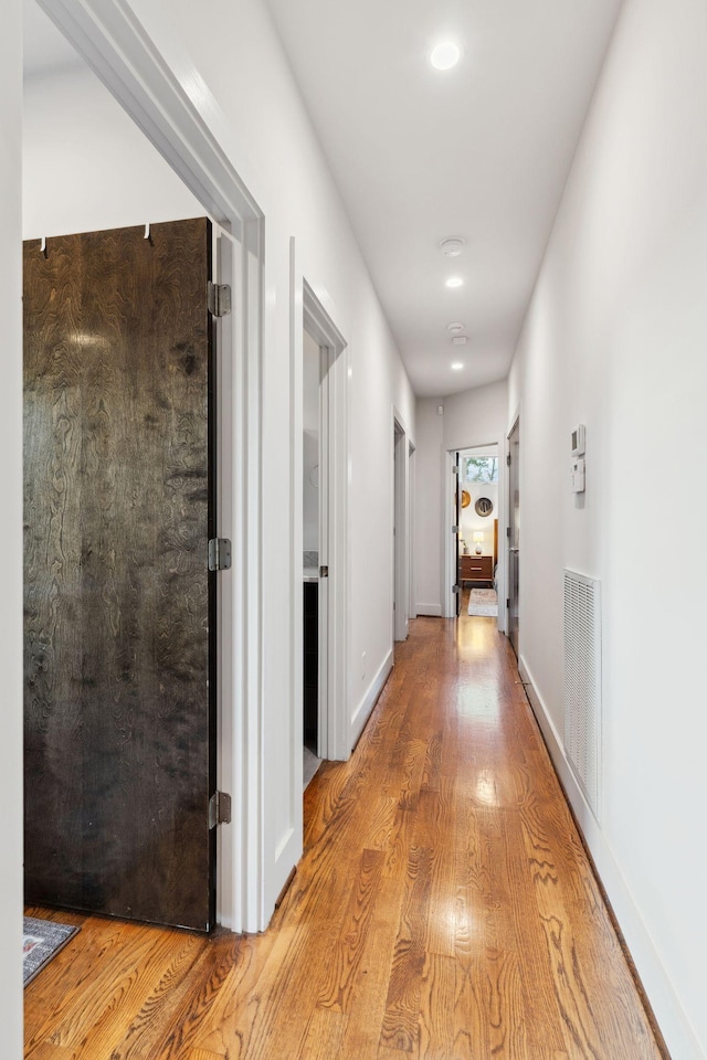 hallway with baseboards, wood finished floors, and visible vents
