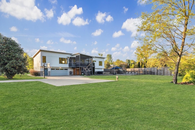 rear view of property featuring an attached garage, a sunroom, fence, and a yard