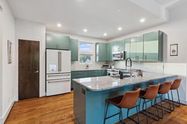 kitchen with a sink, white fridge with ice dispenser, stainless steel microwave, a peninsula, and green cabinetry