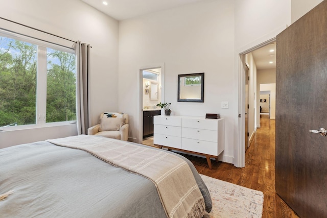 bedroom with baseboards, recessed lighting, wood finished floors, a high ceiling, and connected bathroom