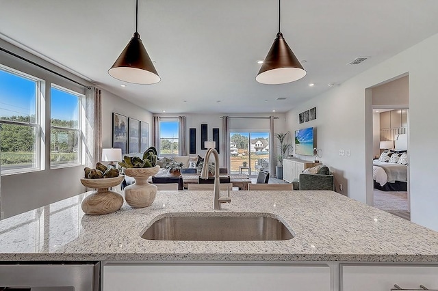 kitchen with open floor plan, light stone countertops, a sink, and hanging light fixtures