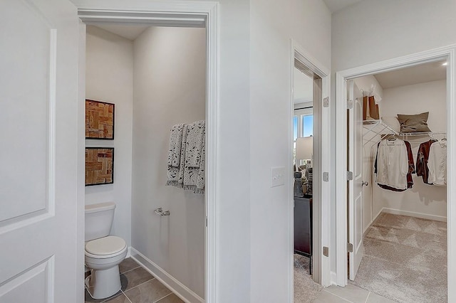 bathroom featuring tile patterned floors, baseboards, a walk in closet, and toilet