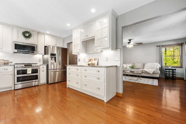 kitchen featuring white cabinetry, decorative backsplash, wood finished floors, ceiling fan, and appliances with stainless steel finishes