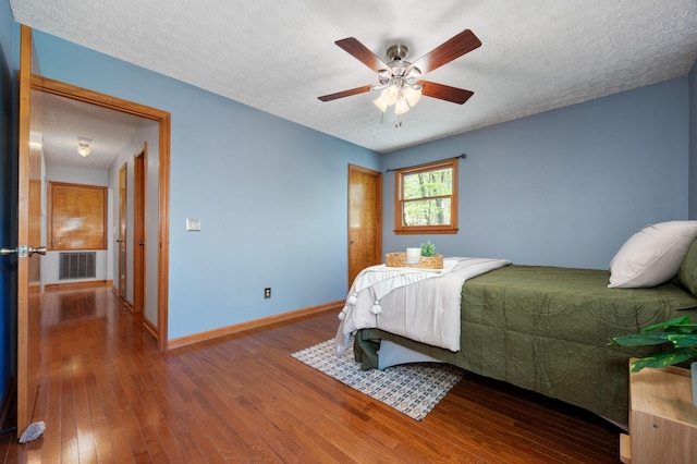 bedroom with hardwood / wood-style floors, baseboards, visible vents, and a textured ceiling