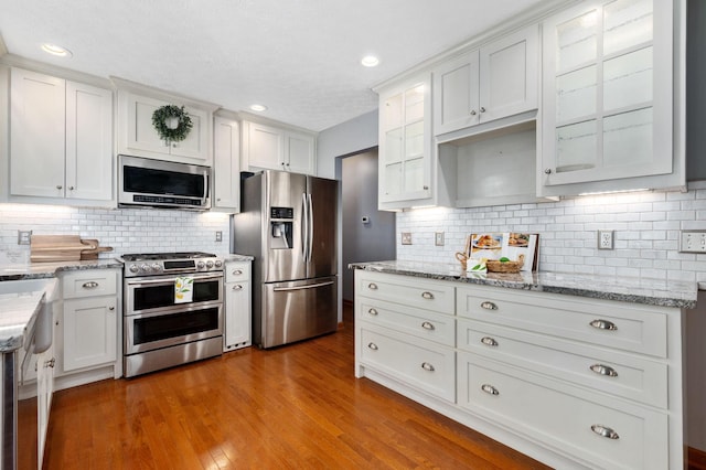 kitchen featuring white cabinets, backsplash, glass insert cabinets, and appliances with stainless steel finishes