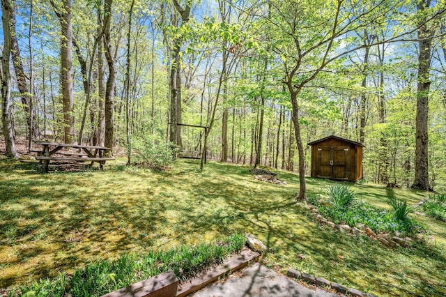 view of yard featuring a forest view, an outdoor structure, and a storage shed