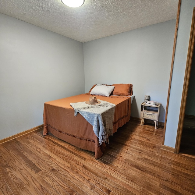 bedroom featuring baseboards, wood finished floors, and a textured ceiling