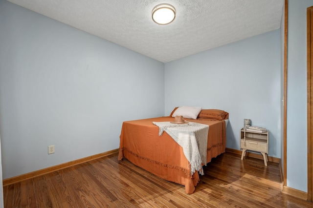 bedroom with baseboards, wood finished floors, and a textured ceiling