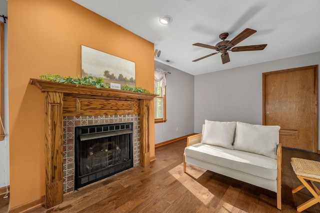 living area featuring a tiled fireplace, visible vents, baseboards, wood finished floors, and ceiling fan