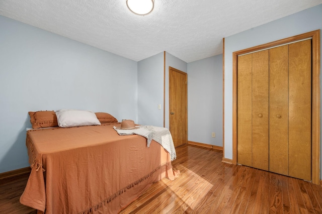 bedroom with baseboards, wood finished floors, a textured ceiling, and a closet