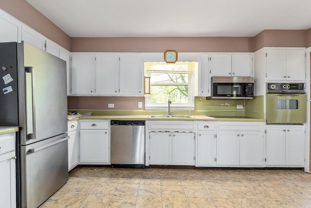 kitchen with white cabinetry, stainless steel appliances, light countertops, and a sink