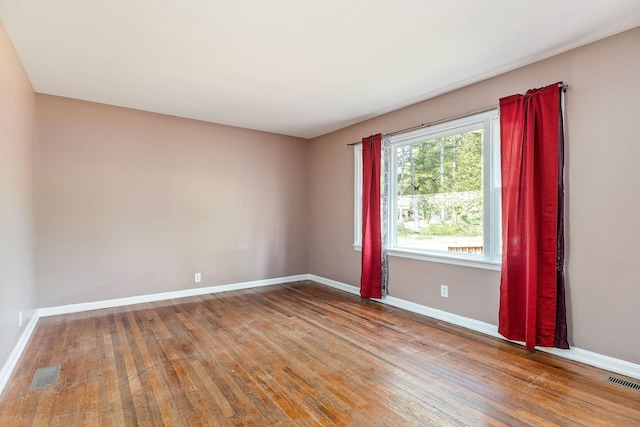 empty room with hardwood / wood-style floors, visible vents, and baseboards