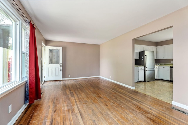 unfurnished living room featuring visible vents, hardwood / wood-style flooring, baseboards, and a wealth of natural light