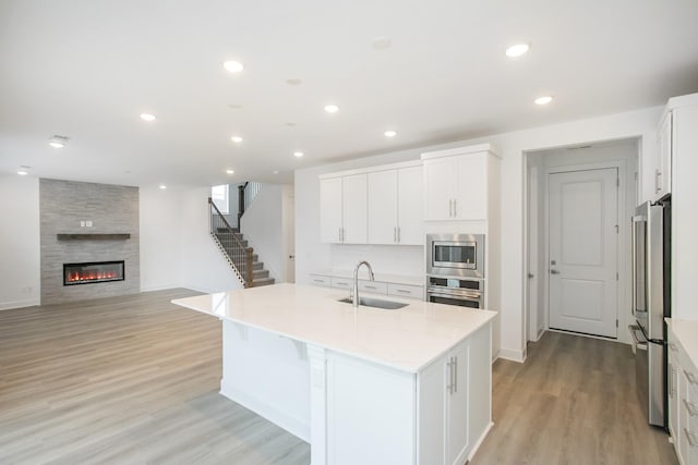 kitchen featuring a sink, stainless steel appliances, white cabinets, a center island with sink, and light wood-type flooring