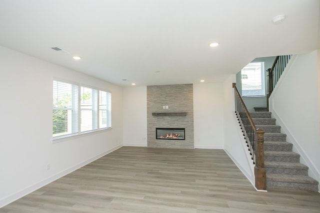 unfurnished living room featuring stairs, light wood-style flooring, a tiled fireplace, and recessed lighting