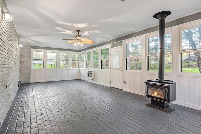 unfurnished sunroom with plenty of natural light, a wood stove, and heating unit