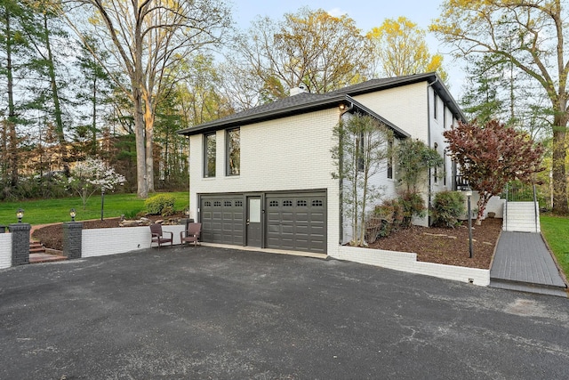view of home's exterior with brick siding, an attached garage, driveway, and a chimney