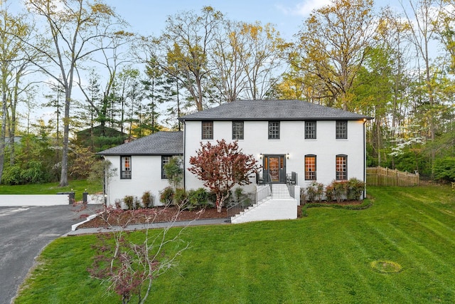 colonial inspired home with fence, driveway, and a front lawn