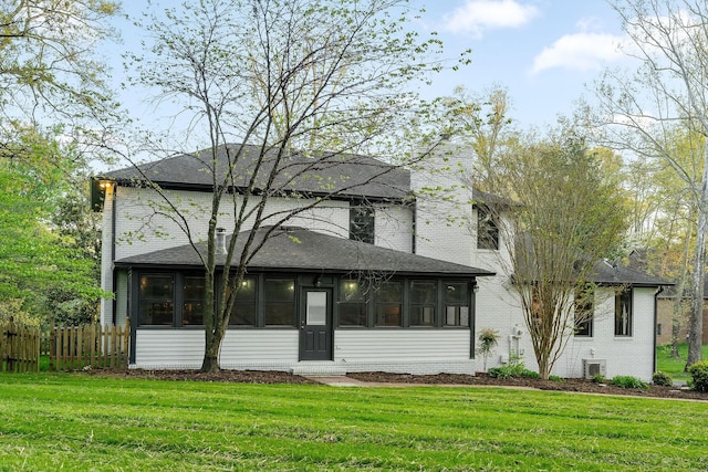prairie-style house featuring a sunroom, fence, a shingled roof, and a front yard