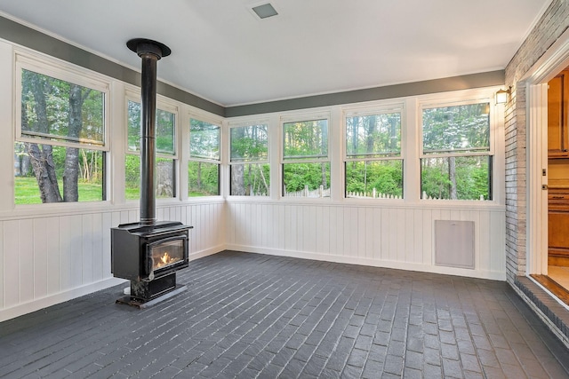 unfurnished sunroom featuring brick floor, plenty of natural light, and a wood stove