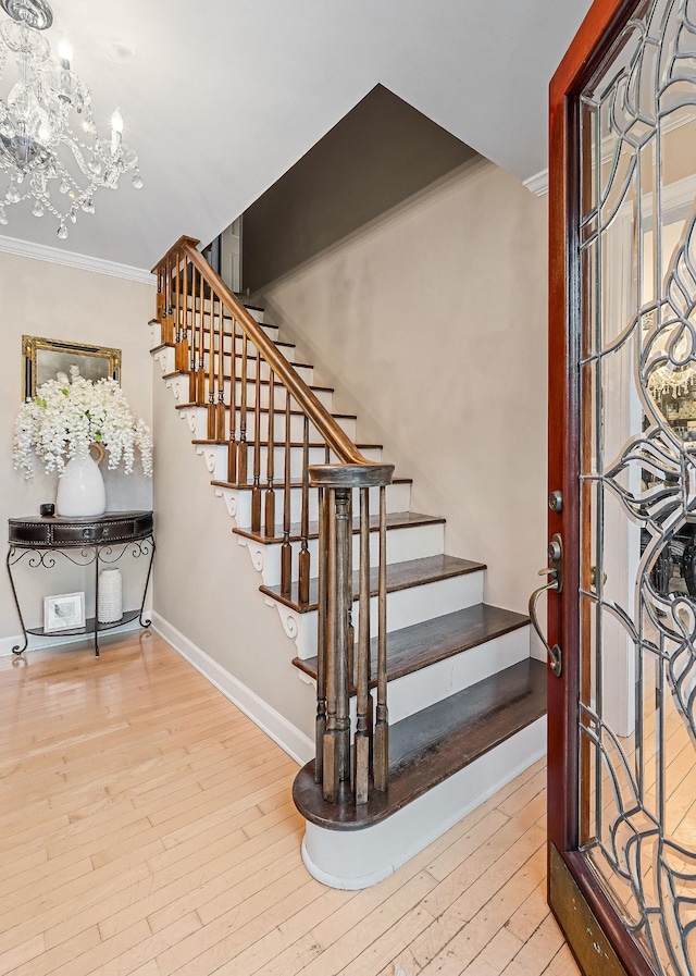 staircase with baseboards, an inviting chandelier, ornamental molding, and wood-type flooring